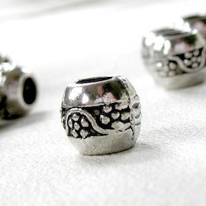 May include: Silver metal bead with a decorative design of grapes and vines. The bead has a smooth, polished finish.