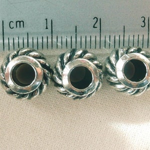 May include: Three silver metal beads with a rope-like design and a hole in the center. The beads are approximately 1 cm in diameter.