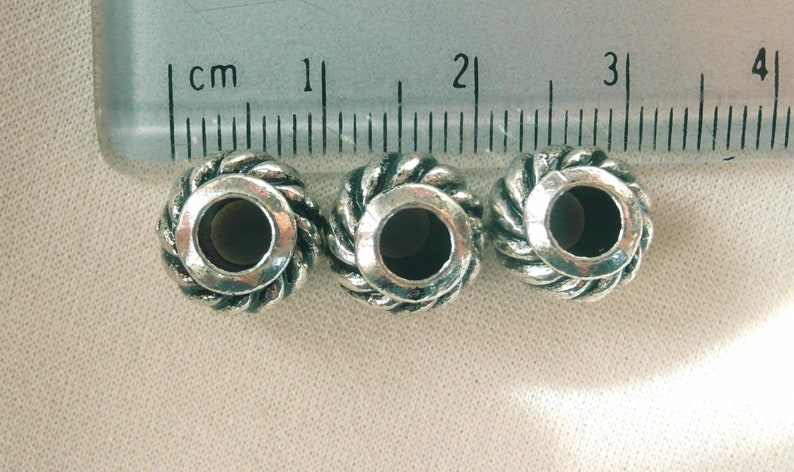 May include: Three silver metal beads with a rope-like design and a hole in the center. The beads are approximately 1 cm in diameter.