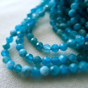 May include: A strand of blue apatite beads, faceted and round, strung on a clear thread. The beads are arranged in a loose, flowing pattern.