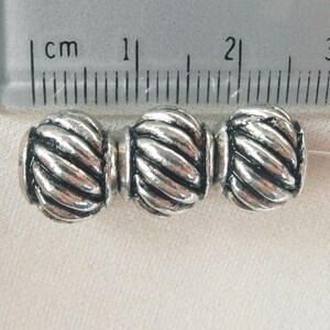 May include: Three silver-toned metal beads with a rope-like design. The beads are approximately 1 cm in diameter.