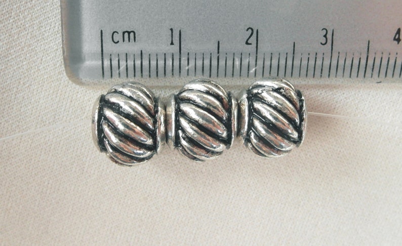 May include: Three silver-toned metal beads with a rope-like design. The beads are approximately 1 cm in diameter.