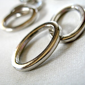 以下が含まれることがあります： 3つの銀色の金属製のリングが互いにつながっているクローズアップ。リングは滑らかで光沢があります。