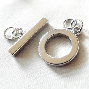 May include: Silver-toned metal toggle clasp with a rectangular bar and a round ring. The clasp is designed for necklaces, bracelets, or other jewelry.