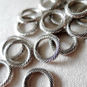 May include: A pile of silver-toned metal rings with a twisted rope design. The rings are all the same size and are arranged in a random pattern.