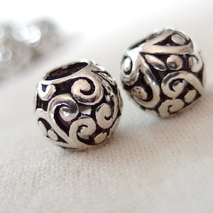 May include: Two silver metal beads with a decorative swirl pattern. The beads are round and have a smooth, polished finish.