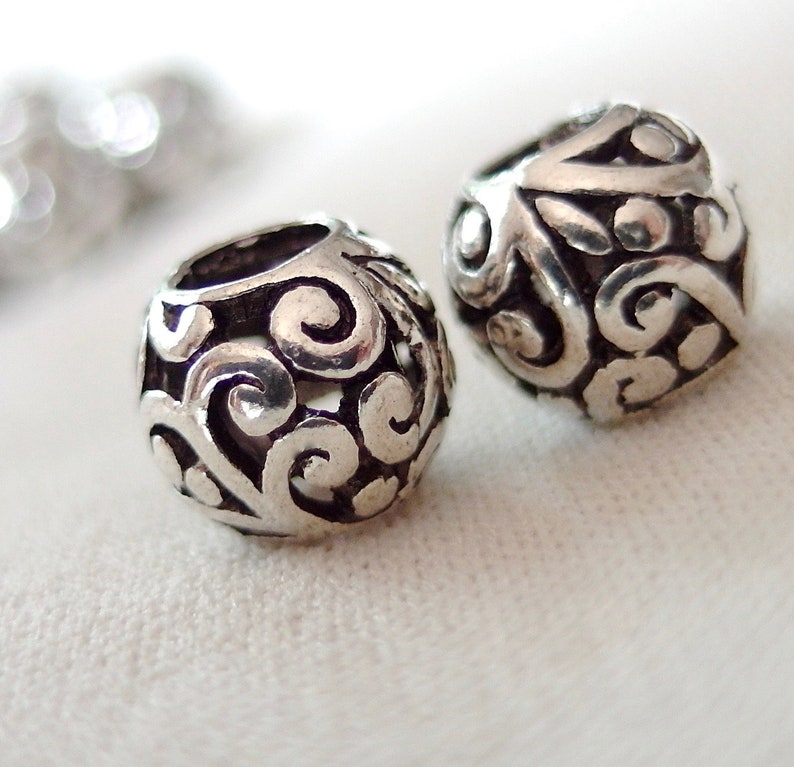 May include: Two silver metal beads with a decorative swirl pattern. The beads are round and have a smooth, polished finish.