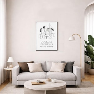 Puede incluir: Un estampado en blanco y negro enmarcado con el texto "Dockside Decisions Were Made" sobre una ilustración de personas en un muelle. El estampado cuelga sobre un sofá gris claro con cojines decorativos. Una mesa de centro redonda y una lámpara de pie están en primer plano.