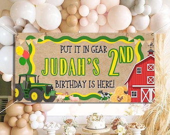 Könnte beinhalten: Ein Banner mit dem Text "PUT IT IN GEAR JUDAH'S 2ND BIRTHDAY IS HERE!" zeigt einen grünen Traktor, eine rote Scheune und Nutztiere. Das Banner ist mit grünen und gelben Akzenten und Luftballons dekoriert. Es ist für eine Geburtstagsparty.