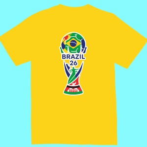 May include: Yellow t-shirt featuring a colorful graphic of a soccer ball and trophy design with the text "BRAZIL 26". The graphic incorporates the colors of the Brazilian flag. The shirt is a short-sleeved crew neck.