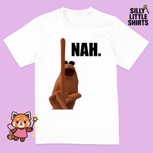 Könnte beinhalten: Weißes T-Shirt mit einer braunen Cartoonfigur, die den Mittelfinger zeigt, und dem Wort "NAH." in Schwarz. Das T-Shirt hat einen Rundhalsausschnitt und kurze Ärmel. Das Markenlogo "SILLY LITTLE SHIRTS" befindet sich in der oberen rechten Ecke.