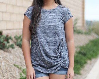 Puede incluir: Una persona joven con una camisa gris y blanca a rayas con un nudo en la parte delantera y pantalones cortos de mezclilla.