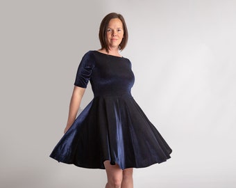 Puede incluir: Una mujer con un vestido de terciopelo azul marino con falda acampanada. El vestido tiene un escote redondo y mangas cortas.