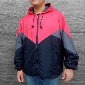 May include: A red, black and grey hooded jacket with a zip fastening. The jacket features a contrasting colour design with a black and grey chevron pattern on the front.