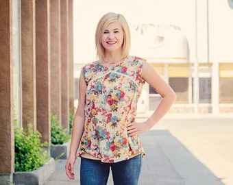 Puede incluir: Una mujer con una blusa de estampado floral sobre fondo beige claro y pantalones vaqueros azules. Está de pie frente a un edificio con columnas. El texto "NEW HORIZONS" es visible en la esquina inferior derecha de la imagen.