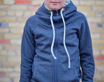 Puede incluir: Una persona joven lleva una sudadera con capucha azul con cremallera y cordones blancos. La sudadera tiene un corte holgado y está hecha de un tejido suave y cómodo.