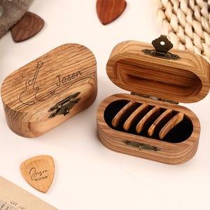 May include: Wooden guitar pick box with a hinged lid, open to reveal guitar picks. The box is engraved with a guitar outline and the name "Jason". A wooden guitar pick with the name "Jason" and the date 05.23.2024 is also visible.