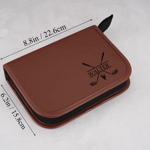 Pode incluir: Uma bolsa marrom para acess&oacute;rios de golfe com z&iacute;per e al&ccedil;a pretos. A bolsa mede 22,6 cm x 15,8 cm. Possui um gr&aacute;fico com tema de golfe e o nome "WALTER" impresso na frente.