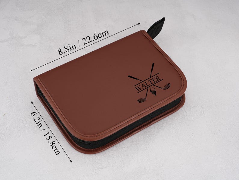 Pode incluir: Uma bolsa marrom para acess&oacute;rios de golfe com z&iacute;per e al&ccedil;a pretos. A bolsa mede 22,6 cm x 15,8 cm. Possui um gr&aacute;fico com tema de golfe e o nome "WALTER" impresso na frente.