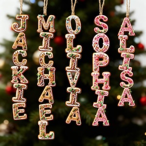May include: Five vertical hanging ornaments shaped like letters spelling the names Jackie, Michael, Olivia, Sophia, and Alisa. The ornaments feature a brown gingerbread texture with white icing details, red and green holly, and candy cane patterns.