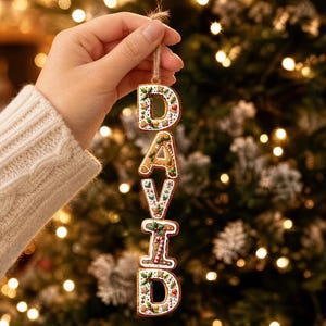May include: A vertical hanging ornament spelling the name DAVID, crafted to resemble gingerbread cookies with white icing details, holly leaves, berries, and candy canes. Each letter is connected by small rings and suspended by a rustic twine loop.