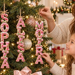 May include: Three vertical hanging Christmas ornaments shaped like gingerbread letters spelling the names SOPHIA, ALISSA, and MOIRA. Each letter features a pink and white icing pattern with small green and red candy accents and a jute twine loop.
