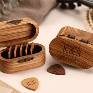 Könnte beinhalten: Zwei Gitarrenplektrum-Boxen aus Holz, eine offen und eine geschlossen, mit mehreren Gitarrenplektren. Auf der geschlossenen Box sind die Initialen "K&S" und das Datum "06-14-2026" eingraviert. Die offene Box enthält mehrere Gitarrenplektren.