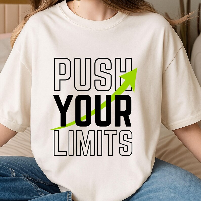 K&ouml;nnte beinhalten: Cremefarbenes T-Shirt mit dem Text "PUSH YOUR LIMITS" in schwarzer Schrift. Ein gr&uuml;ner Pfeil nach oben begleitet den Text. Ein l&auml;ssiges Kleidungsst&uuml;ck f&uuml;r den Alltag.