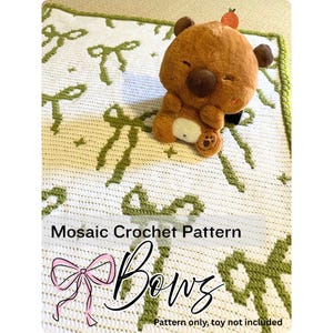 May include: A white mosaic crochet pattern with green bow designs. A brown teddy bear plush toy with a small orange strawberry on its head sits on the blanket. The text "Mosaic Crochet Pattern" and "Bows" is visible.