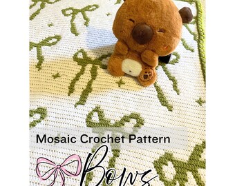 Può includere: Un motivo all'uncinetto a mosaico bianco con disegni di fiocchi verdi. Un peluche a forma di orsetto marrone con una piccola fragola arancione sulla testa è appoggiato sulla coperta. Il testo "Mosaic Crochet Pattern" e "Bows" è visibile.