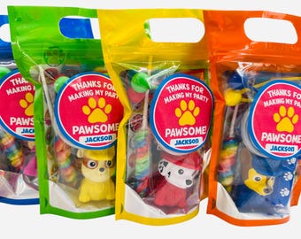 May include: Colorful party favor bags with a Paw Patrol theme. Each bag contains a toy figurine, candy, and a round sticker that says "Thanks for making my party PAWSOME!" with a name.