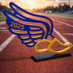 May include: A blue and gold track and field award shaped like a winged running shoe. The year "2025" is displayed on the wing. The award is set on a black base, placed on a red track.