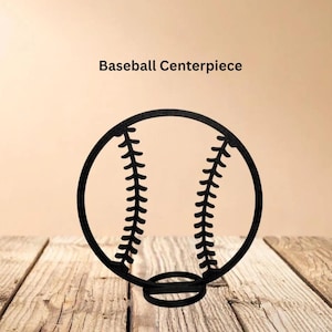 May include: A black, circular baseball centerpiece featuring a cutout design of baseball stitching in the center. The object is mounted on a small, circular base. The text "Baseball Centerpiece" is printed in black above the object.