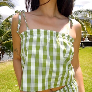 May include: Green and white plaid crop top with tie straps. The top has a square neckline and is paired with matching shorts. The fabric has a classic gingham pattern, perfect for a summer outfit.