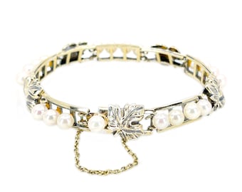 Op de afbeelding: Een gouden armband met een kettingsluiting en een bladontwerp. De armband is versierd met witte parels.