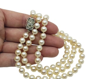 May include: A double-strand pearl necklace with a decorative silver clasp. The pearls are a creamy white color and appear to be of uniform size. The clasp has an ornate design. The necklace is displayed against a white background.
