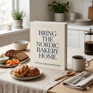 May include: A cookbook titled "Bring the Nordic Bakery Home" with the subtitle "100 Scandinavian Recipes" stands on a wooden table. The image includes baked goods, coffee, and a linen tablecloth, suggesting a culinary theme.