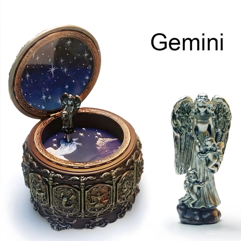 May include: A round, dark brown music box with a hinged lid featuring the text Gemini. The exterior displays relief carvings of zodiac signs. The interior lid and base show a blue starry night sky. A silver-toned angel figurine stands separately.