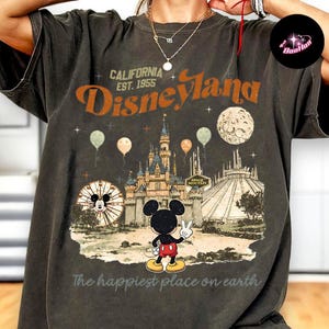 A person wearing a t-shirt with a graphic design depicting Mickey Mouse and various Disney-themed elements, including a castle and balloons.