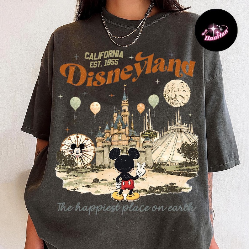 A person wearing a t-shirt with a graphic design depicting Mickey Mouse and various Disney-themed elements, including a castle and a Ferris wheel.