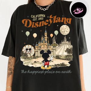 A black t-shirt with a graphic design depicting Mickey Mouse and various Disney-themed elements, including a castle, roller coaster, and balloons.