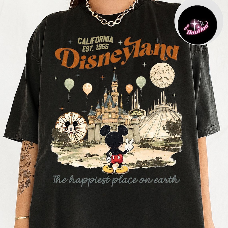 A black t-shirt with a graphic design depicting Mickey Mouse and various Disney-themed elements, including a castle, roller coaster, and balloons.
