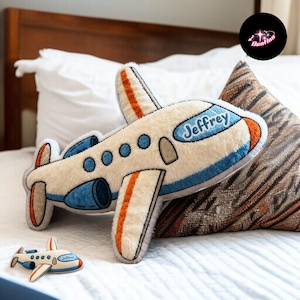 A stuffed airplane toy with the name "Jeffrey" written on it is placed on a bed, surrounded by pillows.