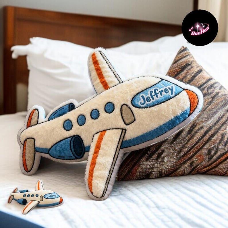 A stuffed airplane toy with the name "Jeffrey" written on it is placed on a bed, surrounded by pillows.