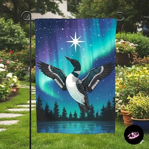 May include: A garden flag featuring a loon with outstretched wings against a backdrop of the aurora borealis. The design includes a starry night sky, a bright star, and a forest silhouette reflected in a lake. The flag is displayed outdoors.