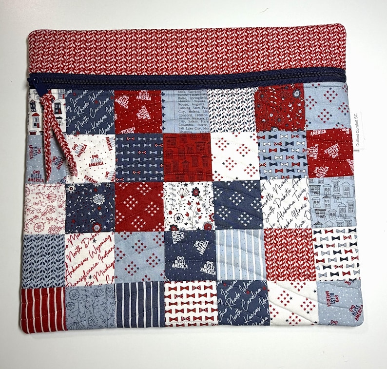 K&ouml;nnte beinhalten: Eine rechteckige, gesteppte Rei&szlig;verschlusstasche mit einem Patchwork-Design aus roten, wei&szlig;en und blauen Stoffquadraten. Die Muster zeigen Staatsnamen, kleine Fliegen, Sterne und Blumenmotive. Ein dunkelblauer Rei&szlig;verschluss verl&auml;uft oben.