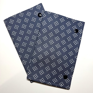 May include: Two navy blue fabric items with a white star pattern. Each item has a black snap closure. The items are likely fabric sleeves or covers, possibly for books or other small objects.