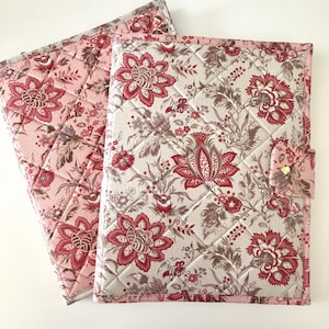 May include: Two quilted fabric covers with floral patterns. One is a light pink with a floral design, and the other is a cream color with a red floral pattern. The covers have a diamond-shaped quilting pattern.