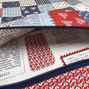 K&ouml;nnte beinhalten: Eine Rei&szlig;verschlusstasche mit einem Patchwork-Au&szlig;enmaterial aus roten, wei&szlig;en und blauen Stoffquadraten, die mit "God Bless America" und verschiedenen Mustern bedruckt sind. Das Innenfutter ist wei&szlig;er Stoff mit Listen von US-Hauptst&auml;dten und Text.