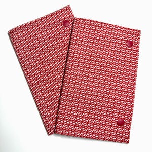 May include: Two rectangular fabric covers featuring a red background with a repeating white leaf or vine pattern. Each cover is secured with a single red snap button located near the top edge, providing a simple closure for these textile items.